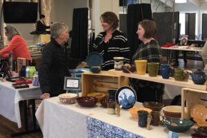Patrons visit and discuss custom pottery and art at a craft and art fair show at the Gold Star Venue at the VFW in Rochester, MN.